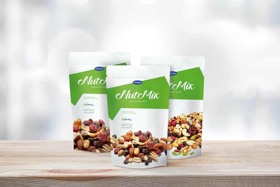 3 stand-up pouches of trail mix on wooden board against grey background
