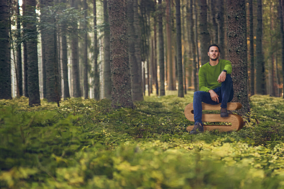 Mann sitzt im Wald auf dem Buchstaben S aus Holz